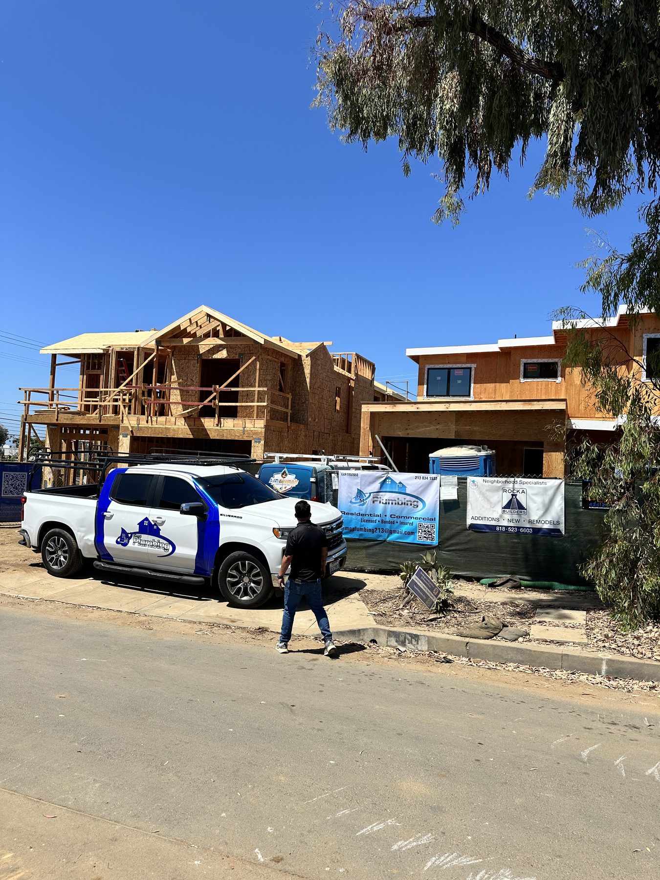 RAMG Plumbing truck, team member, and company banner in front of homes under construction